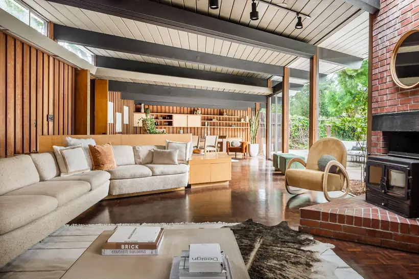 The living room: exposed beams over a plank ceiling, redwood board walls, a brick hearth with a cast-iron stove and parquet flooring opening to the terrace.