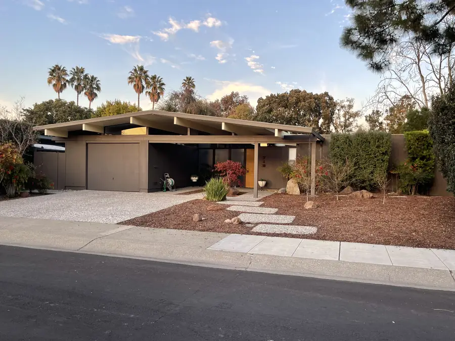 A Los Arboles Eichler at golden hour: deep open carport, a Japanese maple by the entry path, palms and low sun behind the roofline.