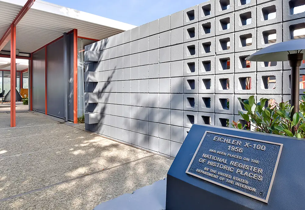 A concrete breeze-block screen wall beside the bronze National Register of Historic Places plaque reading Eichler X-100, 1956.